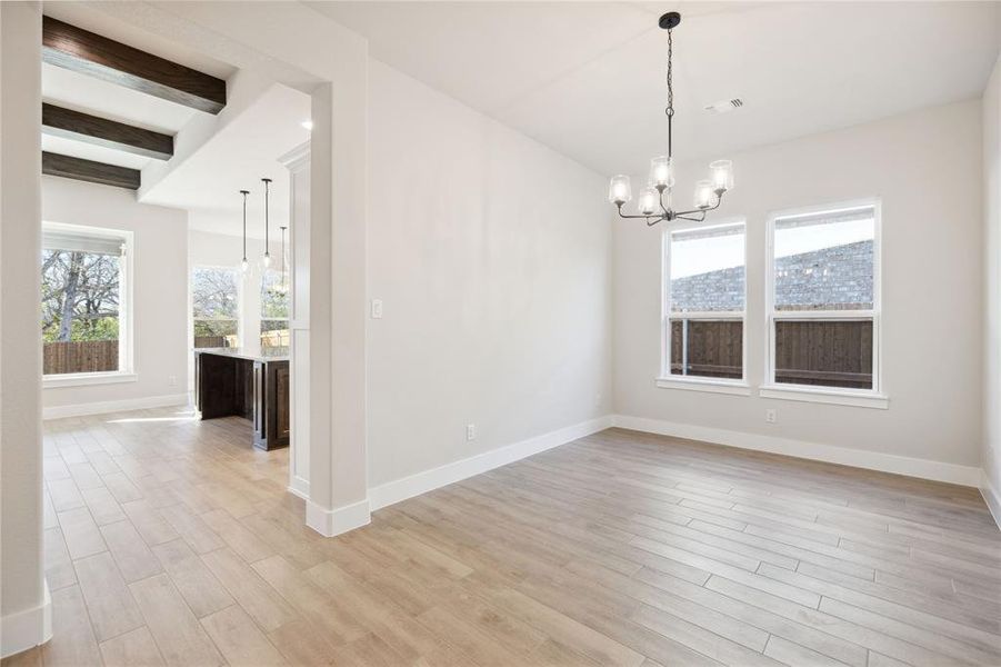 Spare room featuring a chandelier, beam ceiling, and light wood-type flooring