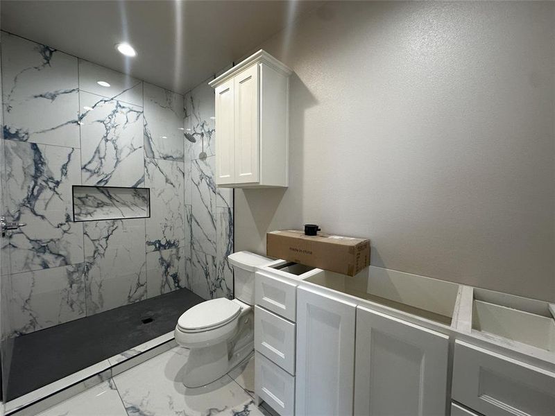 Bathroom featuring a tile shower, vanity, and toilet