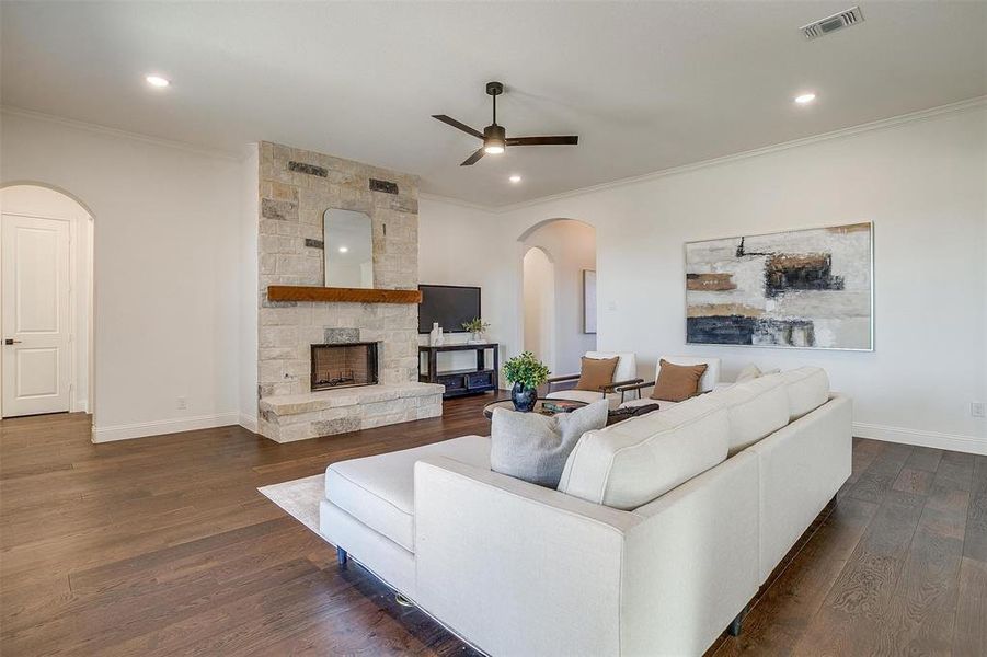 Living room featuring fireplace with stone surround, crown molding, ceiling fan, engineered wood flooring, 10 ft ceilings and 8 ft doors