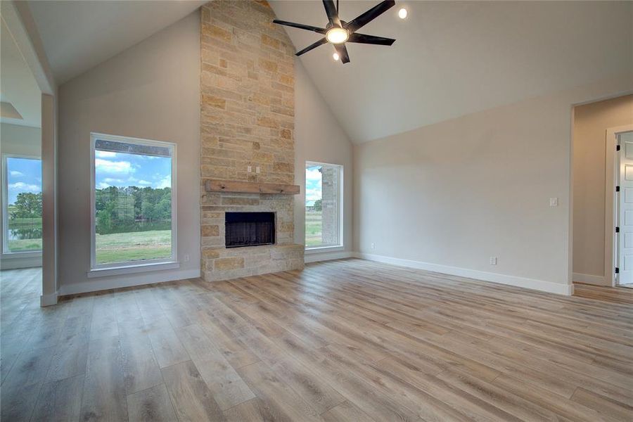 Unfurnished living room featuring high vaulted ceiling, plenty of natural light, light wood-type flooring, and a fireplace