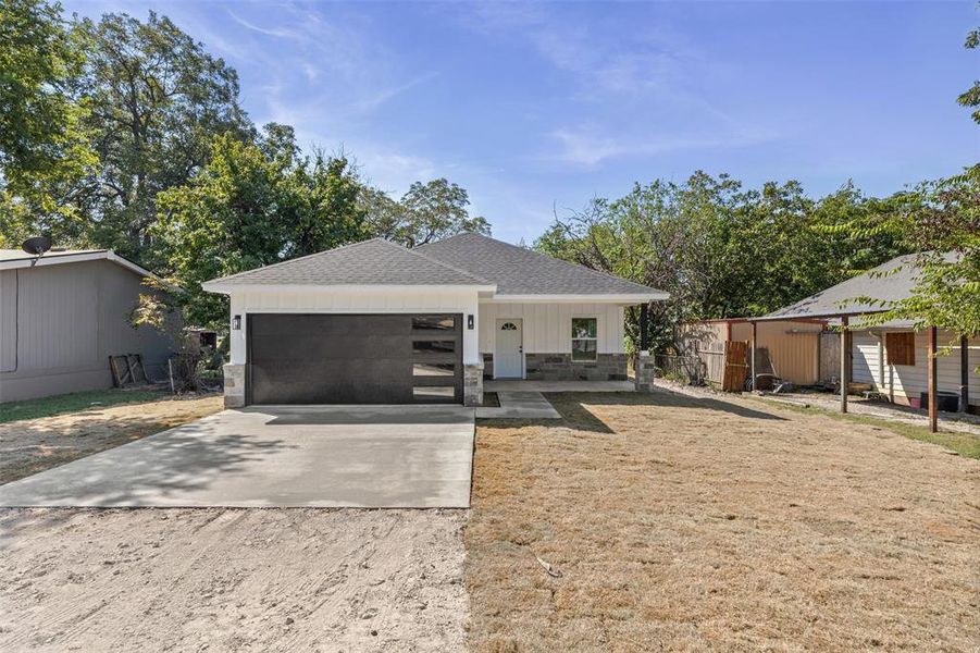 View of front of property with concrete driveway, a shingled roof, stone siding, an attached garage, and board and batten siding