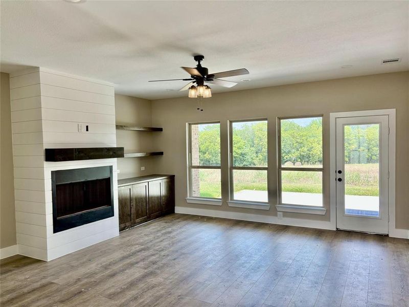 Unfurnished living room with ceiling fan, a large fireplace, and light wood finished floors