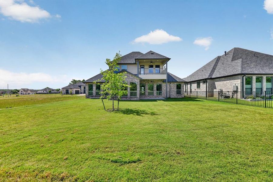 Expansive green lawn surrounds the home, featuring a two-story elevation with a second-level balcony
