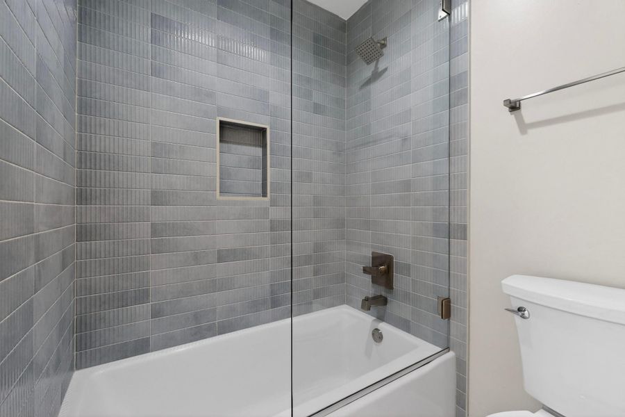 Modern bath features sleek tiled walls, an integrated shower niche, and a glass enclosure.