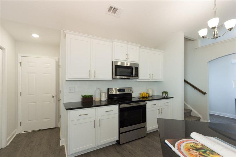 Kitchen featuring appliances with stainless steel finishes, dark hardwood / wood-style floors, a notable chandelier, white cabinets, and tasteful backsplash