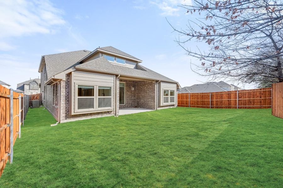 Brick home rear exterior with covered patio, large grassy backyard, and wood privacy fence Brick home rear exterior with covered patio, large grassy backyard, and wood privacy fence