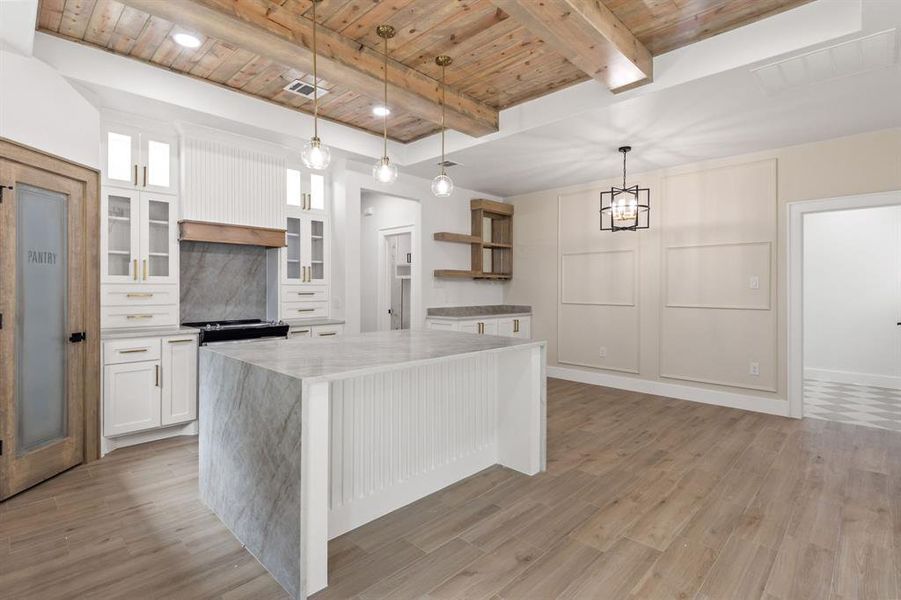 Gourmet kitchen featuring a wood-beam ceiling, white cabinetry, a waterfall-edge island, a pantry door with frosted glass, and wood-finish flooring