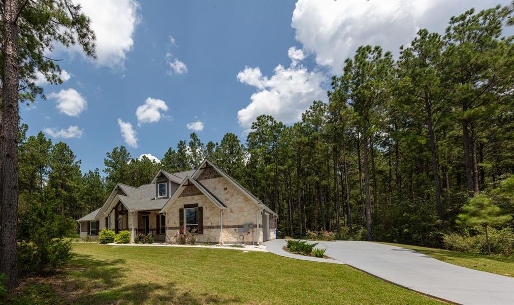 This charming home is nestled among tall pine trees, featuring a stone facade and a welcoming front porch. It offers a spacious driveway and a large front yard, providing a serene and private setting. Perfect for nature lovers seeking tranquility.