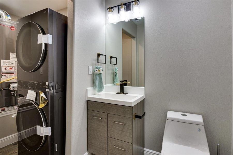 Bathroom featuring vanity, a textured wall, stacked washer and clothes dryer, and gas water heater