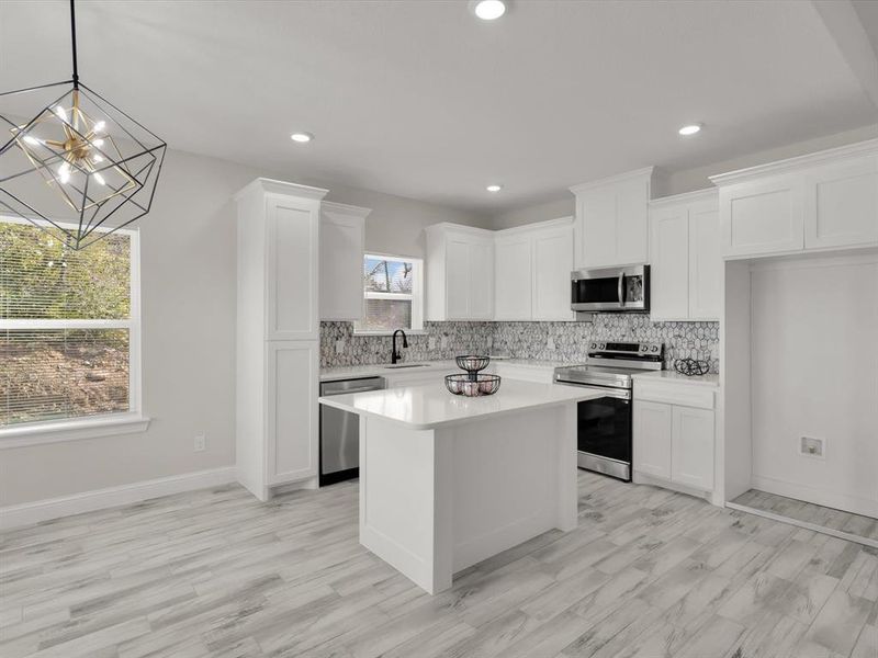 Kitchen featuring stainless steel appliances, sink, pendant lighting, white cabinets, and a center island