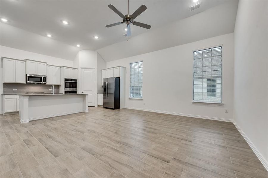 Kitchen featuring ceiling fan, an island with sink, high vaulted ceiling, white cabinetry, and appliances with stainless steel finishes