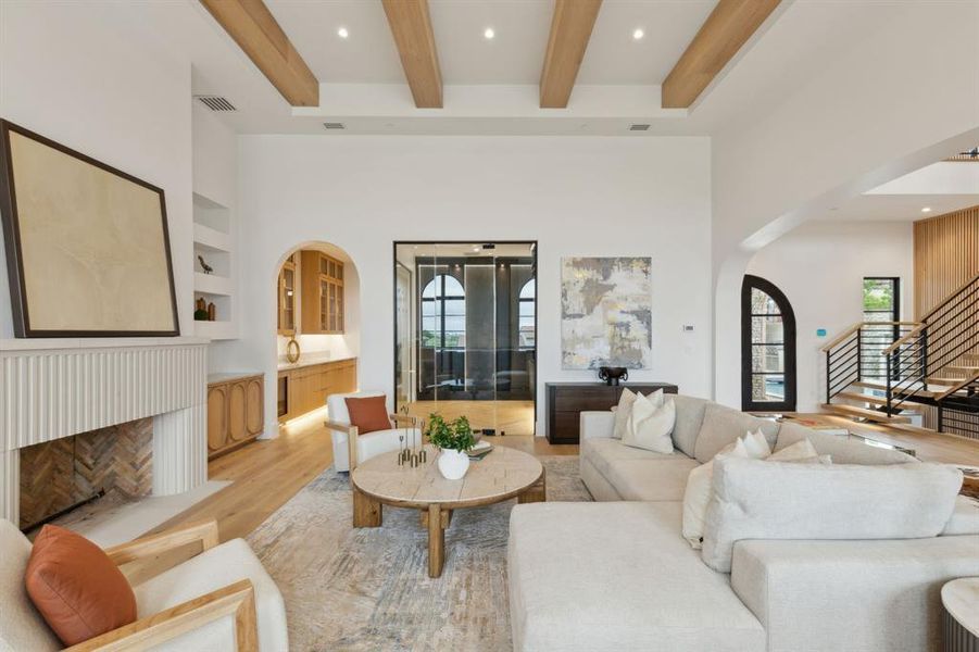 Living area featuring arched walkways, beam ceiling, stairway, white oak wood floors, a wine cellar and a cast stone fireplace Living area featuring arched walkways, beam ceiling, stairway, white oak wood floors, a wine cellar and a cast stone fireplace