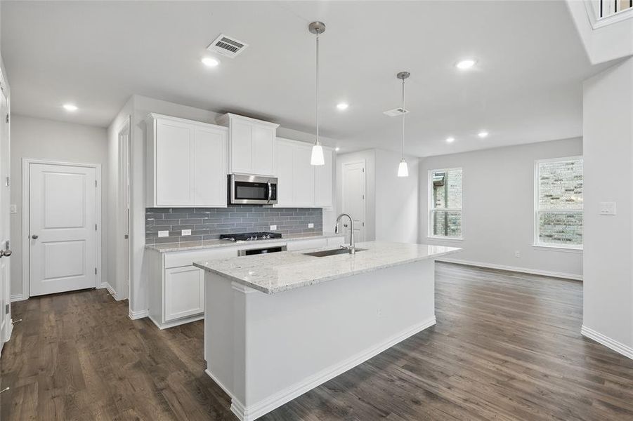Kitchen with decorative backsplash, white cabinetry, decorative light fixtures, light stone countertops, and stainless steel microwave