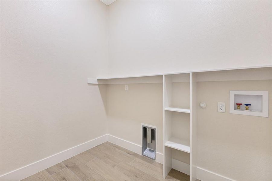 Dedicated utility space featuring built-in shelving, a wall-mounted shelf, a dryer vent, and plumbing hookups