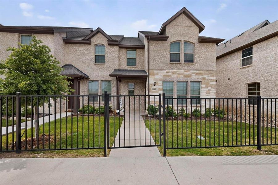 The property features a brick exterior with stone accents, a neatly maintained lawn, and a black wrought iron fence with a gate