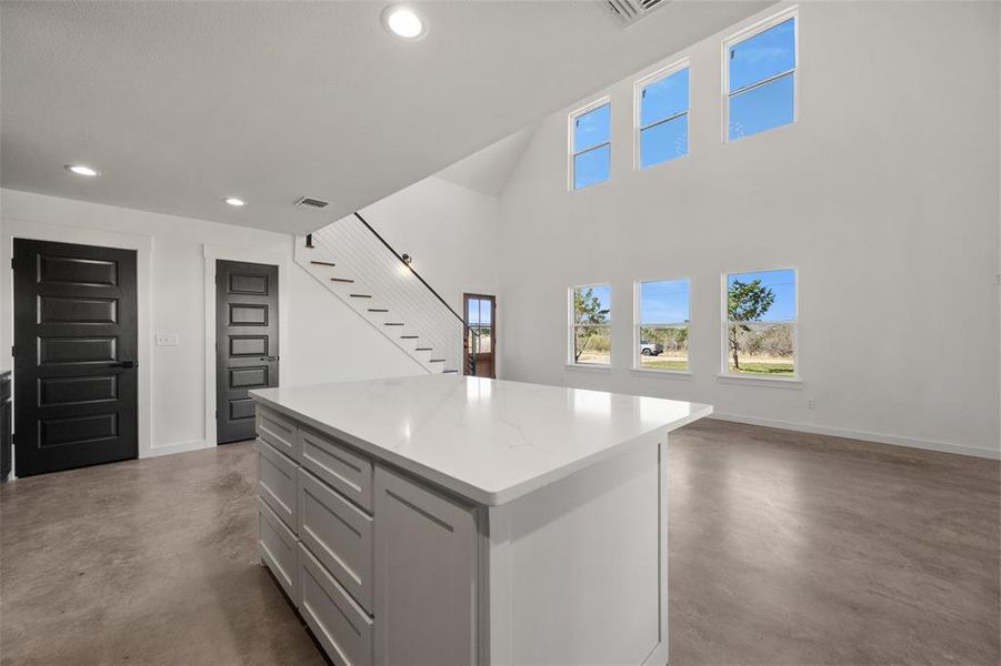 Kitchen with a center island, finished concrete floors, open floor plan, a high ceiling, and light stone countertops