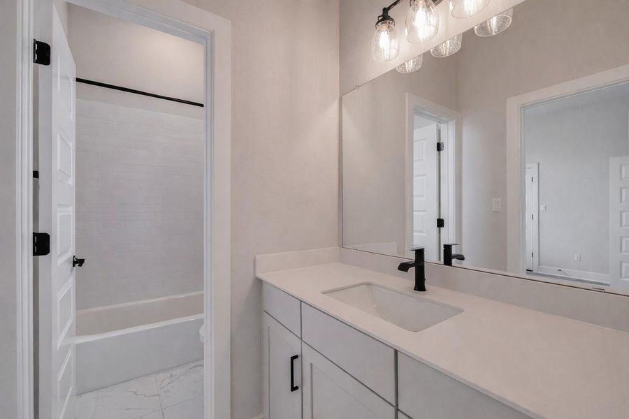 Bathroom featuring a vanity with a white countertop and a rectangular undermount sink, a large mirror, and a light fixture with clear glass shades