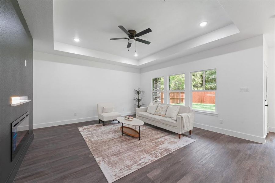 Spacious living area featuring wood-finish flooring, a tray ceiling with recessed lighting, and a ceiling fan Spacious living area featuring wood-finish flooring, a tray ceiling with recessed lighting, and a ceiling fan