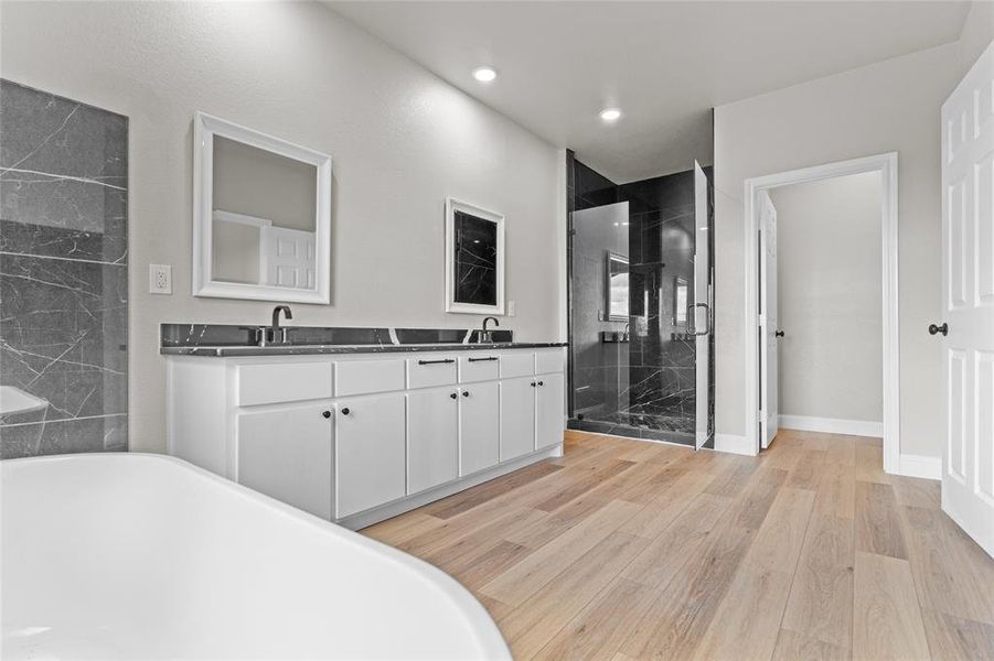 Full bath with double vanity, a shower stall, light wood-type flooring, a soaking tub, and recessed lighting