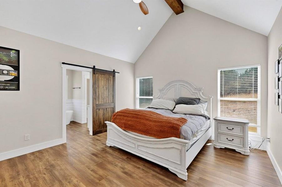 Bedroom featuring a barn door, high vaulted ceiling, beam ceiling, ceiling fan, and wood finished floors
