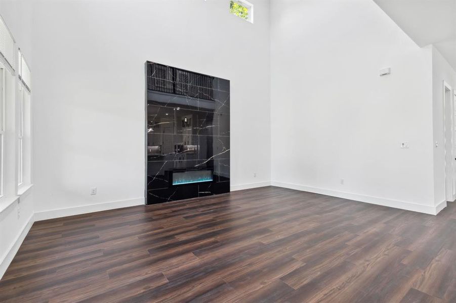 Unfurnished living room featuring dark wood-type flooring and a towering ceiling