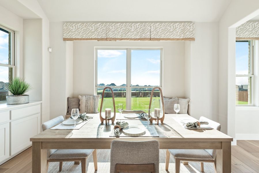 Bright dining area with wood table, bench seating, and large windows overlooking a backyard