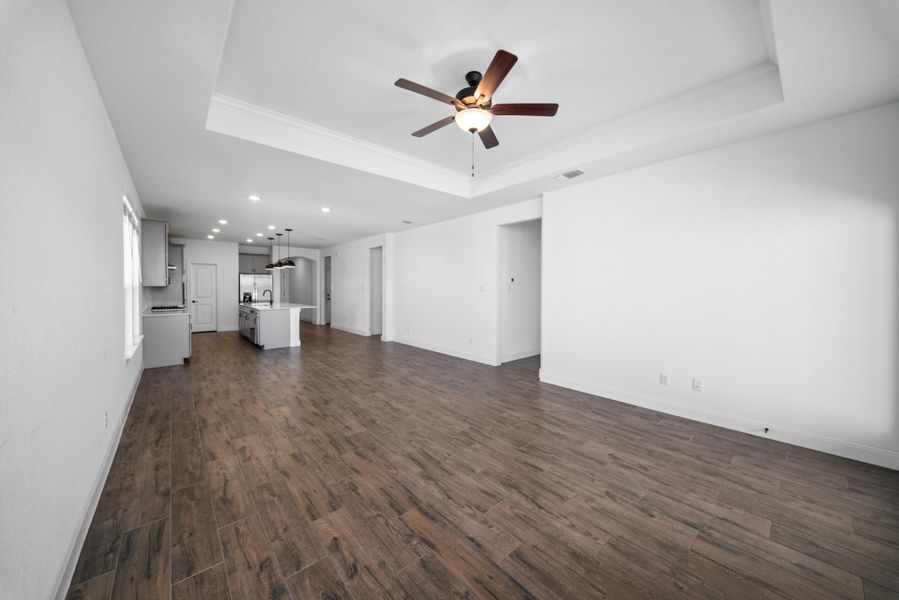 Unfurnished living room with a raised ceiling, dark wood-type flooring, ornamental molding, and ceiling fan Unfurnished living room with a raised ceiling, dark wood-type flooring, ornamental molding, and ceiling fan