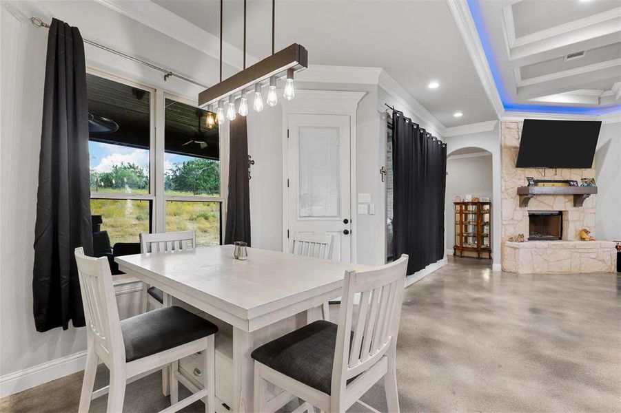 Dining space with crown molding, a stone fireplace, and concrete flooring