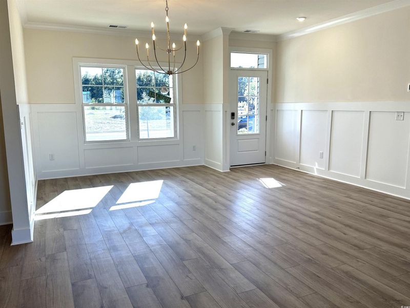 Unfurnished dining area featuring a decorative wall, a chandelier, a wainscoted wall, dark wood-style flooring, and crown molding