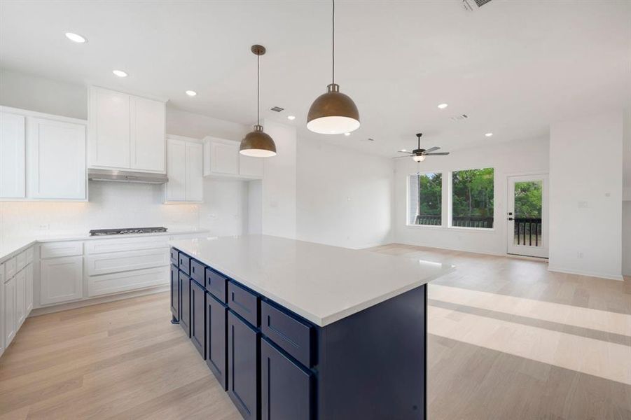 Open-concept living space featuring a spacious kitchen island with dark cabinetry, white perimeter cabinetry, and light wood-finish flooring