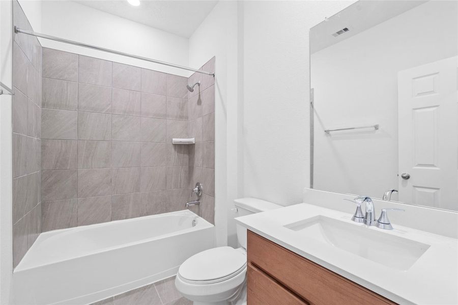 The secondary bathroom showcases tile flooring, a bath/shower combo with a Daltile tile surround, a 30" vanity with a stunning light countertop, a mirror, sleek fixtures, and contemporary finishes throughout.