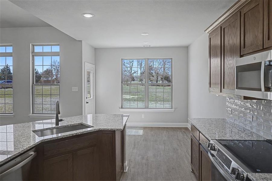 Kitchen featuring stainless steel appliances, light stone counters, dark wood finish cabinets, light wood finished floors, and recessed lighting