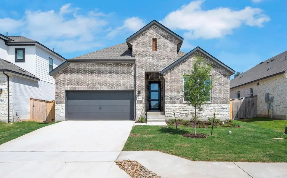 French country style house with a garage, brick siding, driveway, and stone siding