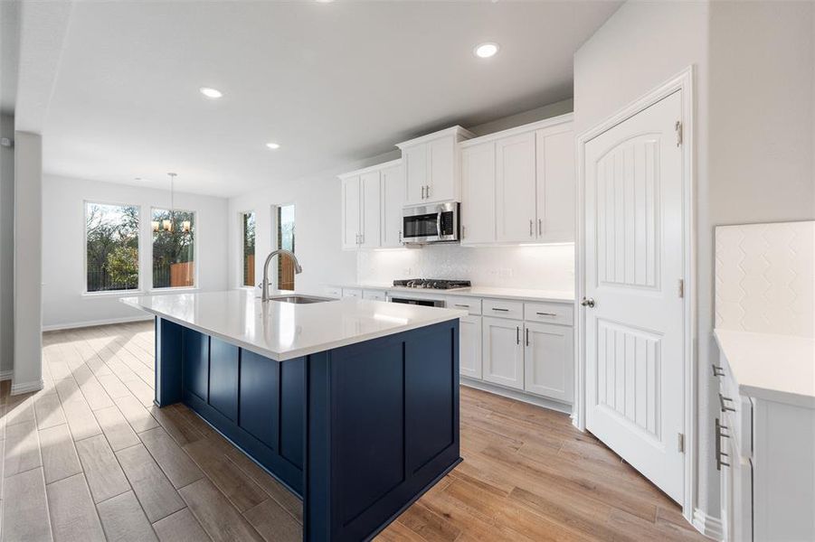 Kitchen featuring decorative backsplash, white cabinetry, a kitchen island with sink, hanging light fixtures, and light wood-style flooring