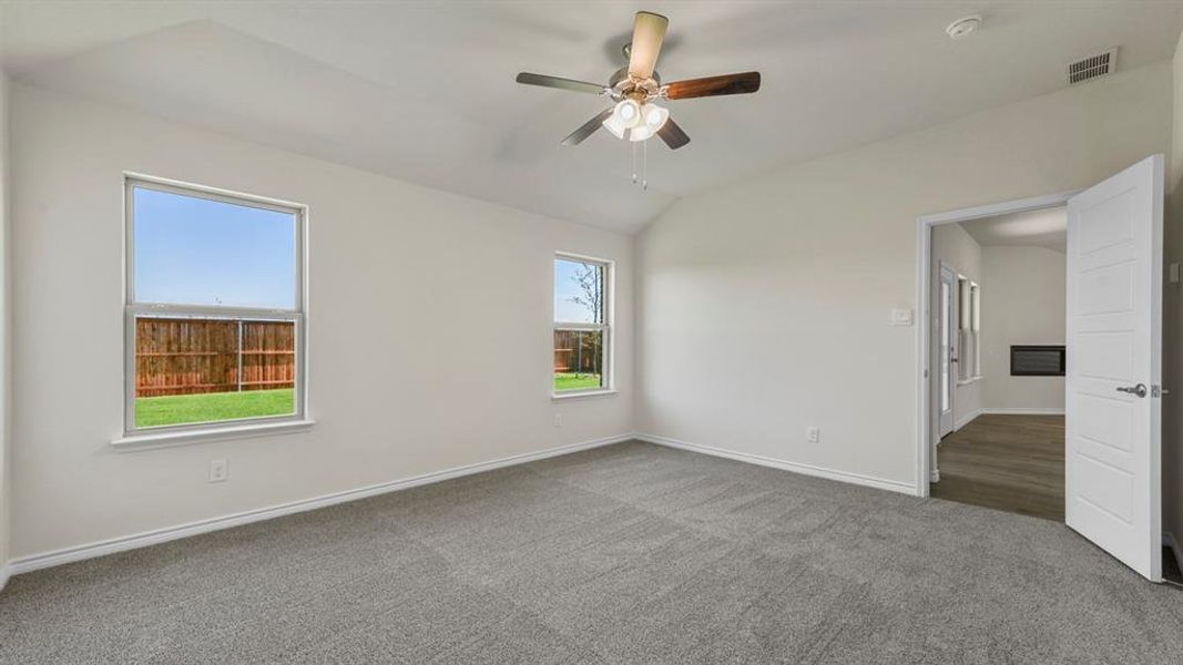 Spacious room featuring vaulted ceilings, a ceiling fan with integrated lighting, and two windows providing views of the backyard