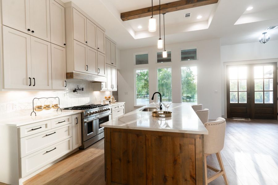 Kitchen featuring double oven range, light wood-type flooring, backsplash, an island with sink, and decorative light fixtures Kitchen featuring double oven range, light wood-type flooring, backsplash, an island with sink, and decorative light fixtures