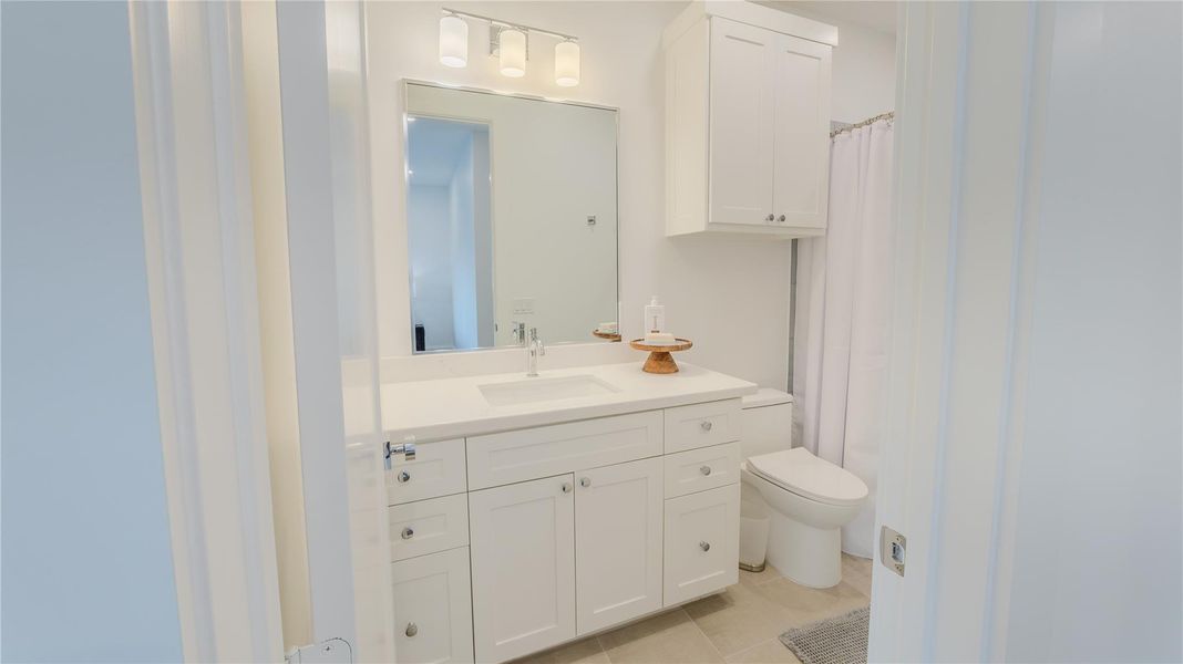 This bathroom features a clean, modern design with white cabinetry and a spacious countertop. It includes a large mirror, overhead lighting, and a shower with a curtain, creating a bright and functional space.