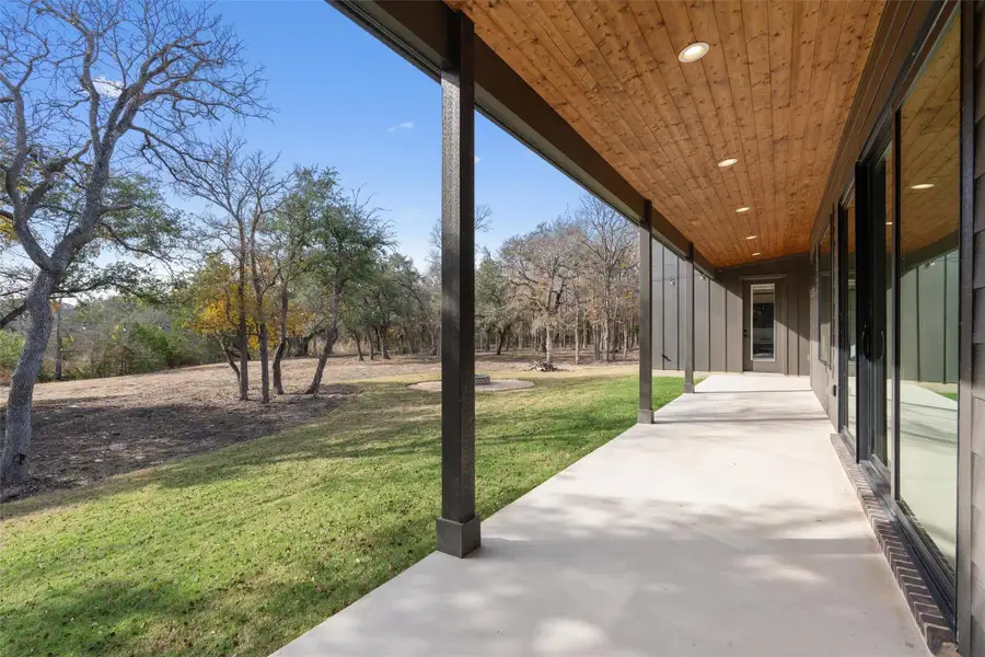An inviting covered patio extends along the modern exterior, offering a peaceful view of the wooded natural landscape. An inviting covered patio extends along the modern exterior, offering a peaceful view of the wooded natural landscape.