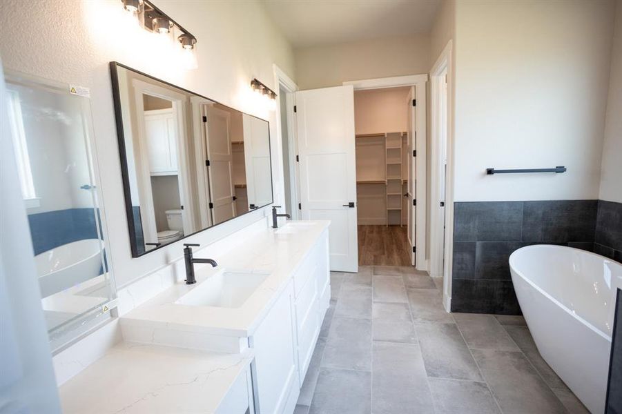 Full bath with a freestanding bath, a walk in closet, double vanity, and tile walls Full bath with a freestanding bath, a walk in closet, double vanity, and tile walls