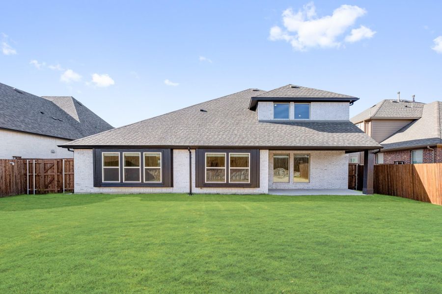 Rear exterior of two-story brick home with large fenced backyard and green lawn Rear exterior of two-story brick home with large fenced backyard and green lawn
