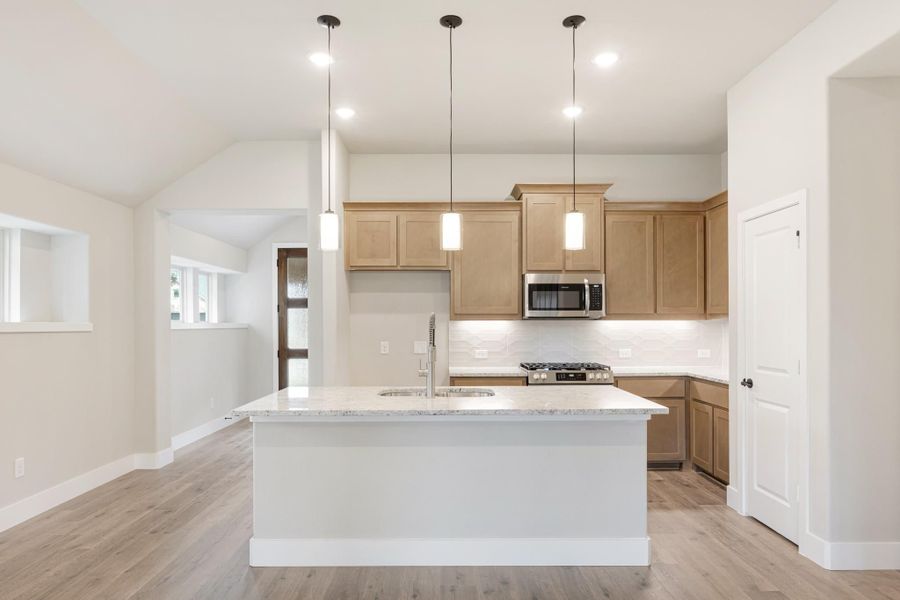 Kitchen with large island, granite countertops, light wood cabinets, stainless appliances, and three pendant lights