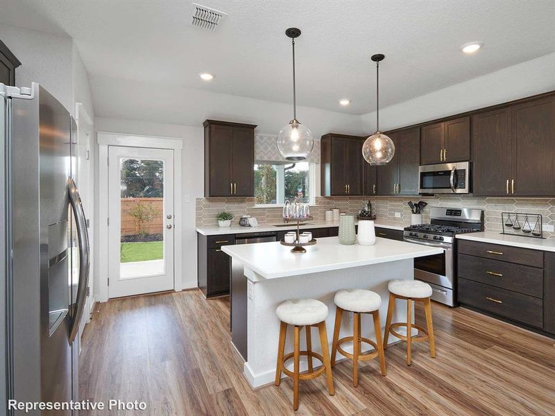 The kitchen features dark wood cabinetry, stainless steel appliances, and a central island with a white countertop