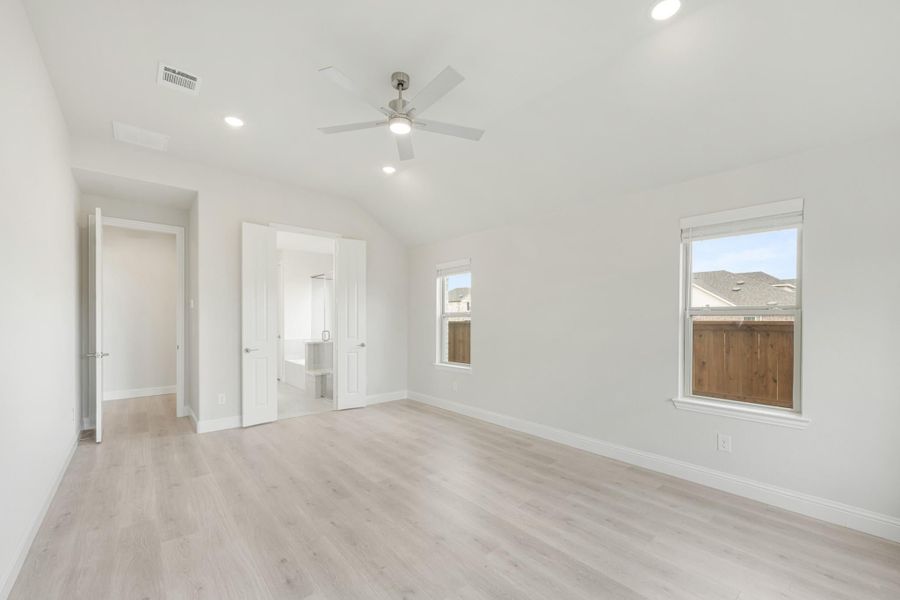 Empty bedroom with vaulted ceiling, ceiling fan, light wood floors, and ensuite bathroom doorway
