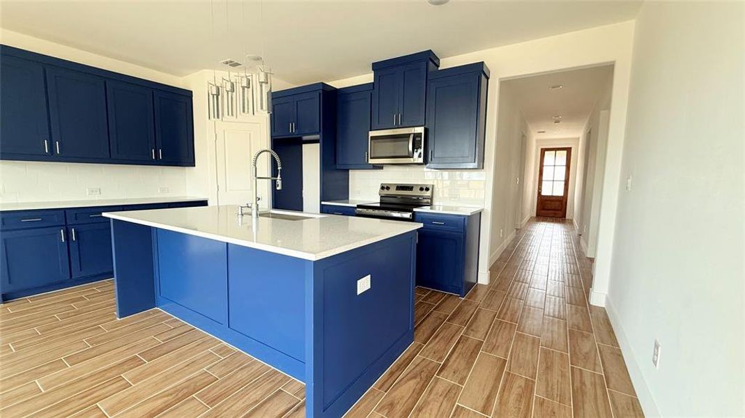 Kitchen with blue cabinetry, wood tiled floor, light countertops, appliances with stainless steel finishes, and a sink