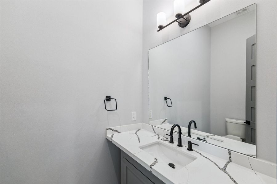 Quartz counters with striking veining and matte black fixtures bring a modern touch to the powder bath. A spacious mirror and wall-mounted lighting ensure a bright, inviting atmosphere that balances practicality with style. Quartz counters with striking veining and matte black fixtures bring a modern touch to the powder bath. A spacious mirror and wall-mounted lighting ensure a bright, inviting atmosphere that balances practicality with style.