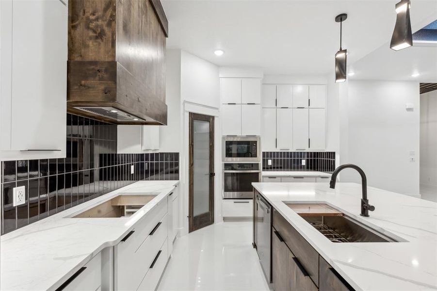 Kitchen featuring sink, light stone counters, appliances with stainless steel finishes, ventilation hood, and decorative backsplash