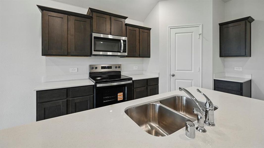 Modern kitchen featuring dark wood cabinetry, white countertops, a stainless steel microwave, and a double basin sink with a chrome faucet