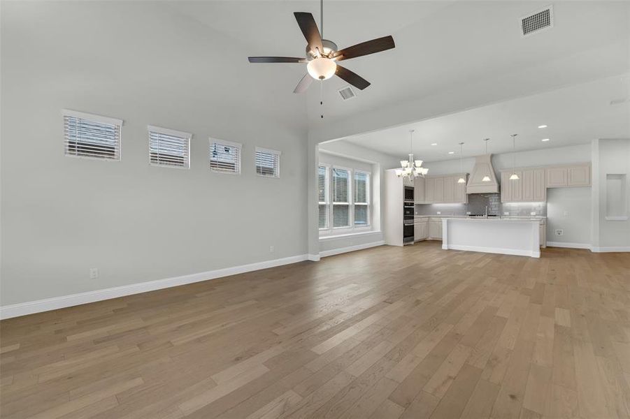 Unfurnished living room featuring hanging lights, ceiling fan, light wood-style floors, and a high ceiling