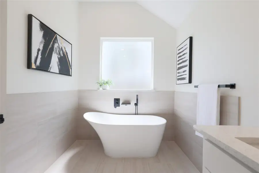 Bathroom featuring tile walls, vanity, a soaking tub, wainscoting, and vaulted ceiling
