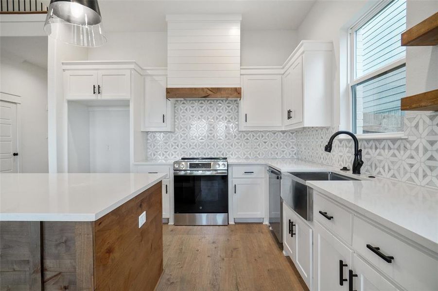 Kitchen featuring appliances with stainless steel finishes, white cabinets, decorative backsplash, light wood-type flooring, and custom exhaust hood